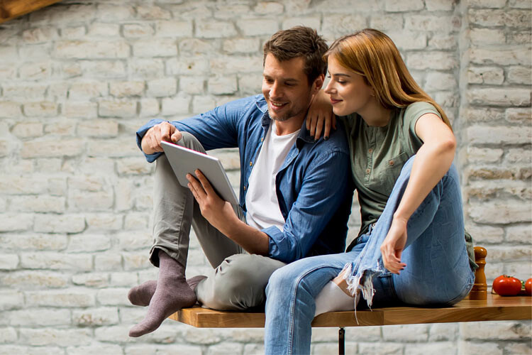 Junger Mann und Frau sitzen auf einer Bank und schauen sich etwas auf einem Tablet an