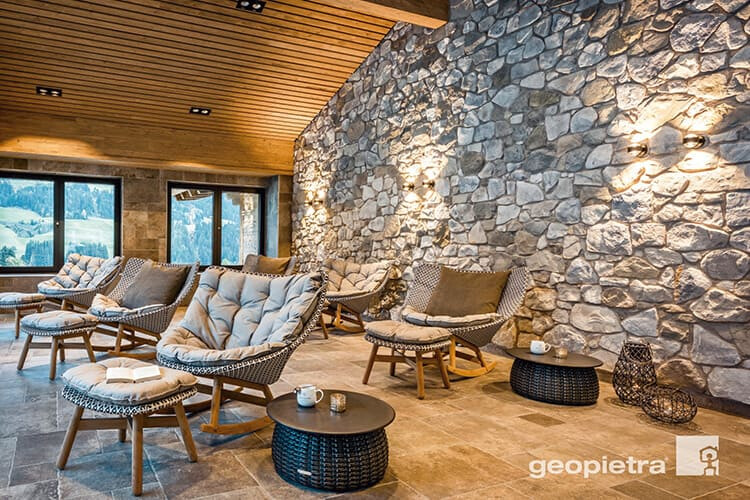 Verlegemuster Polygonalverband in einer Berghütte mit mit mehreren Sitzmöglichkeiten in entspannter Atmosphäre & mit einer Steinwand sowie Fenstern im Hintergrund