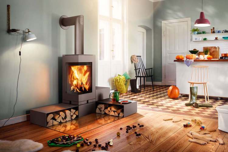 skantherm Kamin im Wohnzimmer mit zwei Regalen, in denen Kaminholz bereitliegt, Spielzeug auf dem Fußboden und einer offenen Küche im Hintergrund